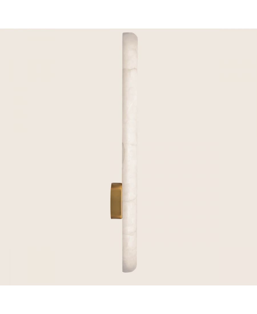 A minimalist wall-mounted light fixture featuring a long, vertical cylindrical diffuser made from translucent white onyx, accented by a small, rectangular brass element mounted on its side. — 3D model