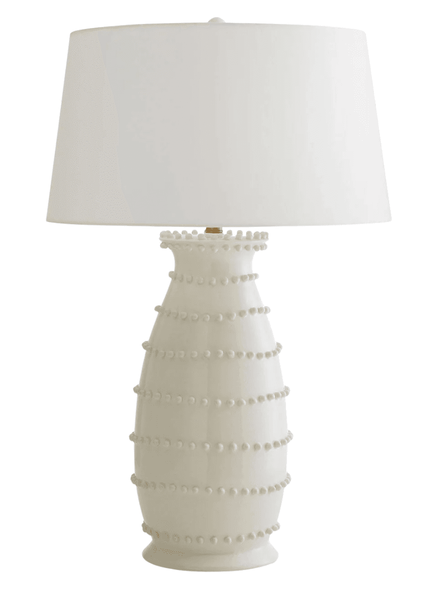 An off-white ceramic table lamp featuring a tapered, vase-like base adorned with horizontal rows of raised, small ceramic beads. The lamp is topped with a classic conical white fabric lampshade, secured by a brass-finished finial. The overall design suggests a contemporary or transitional aesthetic, emphasizing texture and a neutral color palette. — 3D model