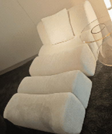 A modern, minimalist chaise lounge featuring a segmented design, upholstered in a textured, off-white bouclé fabric. It has an integrated backrest and is accompanied by a small, matching throw pillow. — 3D model