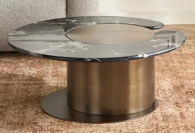 A contemporary coffee table featuring an irregularly shaped black marble top with white veining. The tabletop includes a central circular brushed metallic insert designed to swivel. The entire top is supported by a large, brushed brass cylindrical base, which in turn rests on a flat, circular black metal plate. — 3D model