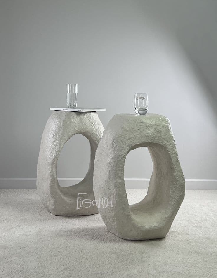 A stool with an abstract, sculptural form. It features a solid, roughly shaped body with a large, irregular opening in the center, suggesting it is designed to be sat upon or used as a small side table. The surface texture is uneven, indicating a material that has been molded or layered. — 3D model