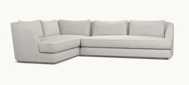 A modern sectional sofa with a light beige fabric upholstery. The sofa features a chaise lounge on the left and a sofa section on the right, with loose back cushions. The design is minimalist with clean lines and a low profile, supported by subtle metallic legs. — 3D model
