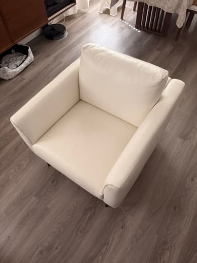 A modern white sofa with a tufted backrest and armrests, upholstered in a material that appears to be faux leather or high-quality vinyl. It features a clean, minimalist design with slim, black metal legs. The stitching detail is visible along the edges. — 3D model