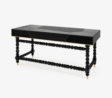 A rectangular console table featuring a glossy black finish with a segmented, geometric top surface. The apron beneath the top has a gold-toned trim. The table is supported by four ornately turned black legs, connected by similarly turned stretchers. The legs terminate in brass-colored feet. — 3D model