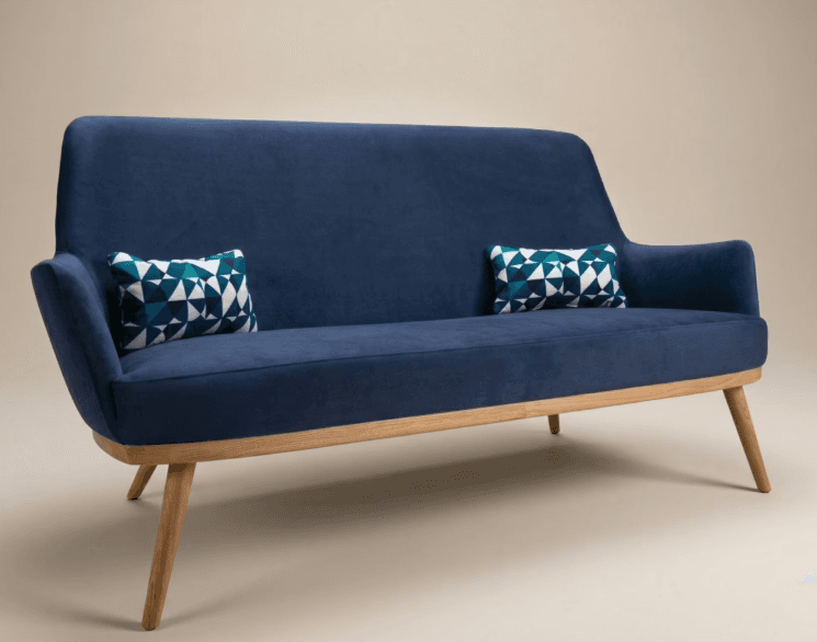 A two-seater sofa with blue upholstery and a visible wooden frame and legs. The design features a gently curved backrest and integrated armrests. Two small accent pillows with a geometric pattern are placed on the sofa. — 3D model