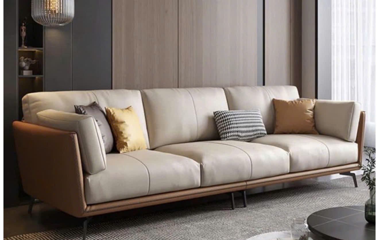 A modern three-seater sofa featuring a two-tone design with light beige/cream main upholstery on the seat and back cushions, contrasted by brown panels on the armrests and lower back. The sofa is supported by slender, dark-finished metal legs and includes several accent throw pillows in varying colors and patterns. — 3D model