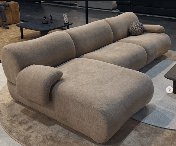A modular sectional sofa with a chaise lounge. The sofa features rounded, organic shapes with deep seating and plush cushions. It has a low profile and is upholstered in a textured fabric. — 3D model