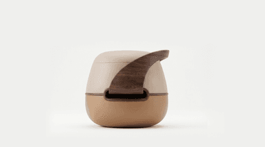 A compact, round, contemporary stool or ottoman. It features a two-tone upholstered body, with a lighter beige on the upper section and a warmer caramel brown on the lower, bulbous base. A thin wooden trim separates the two leather sections. A prominent, curved wooden handle in a dark wood tone arches gracefully over the top, creating a sculptural element and an opening beneath it. — 3D model