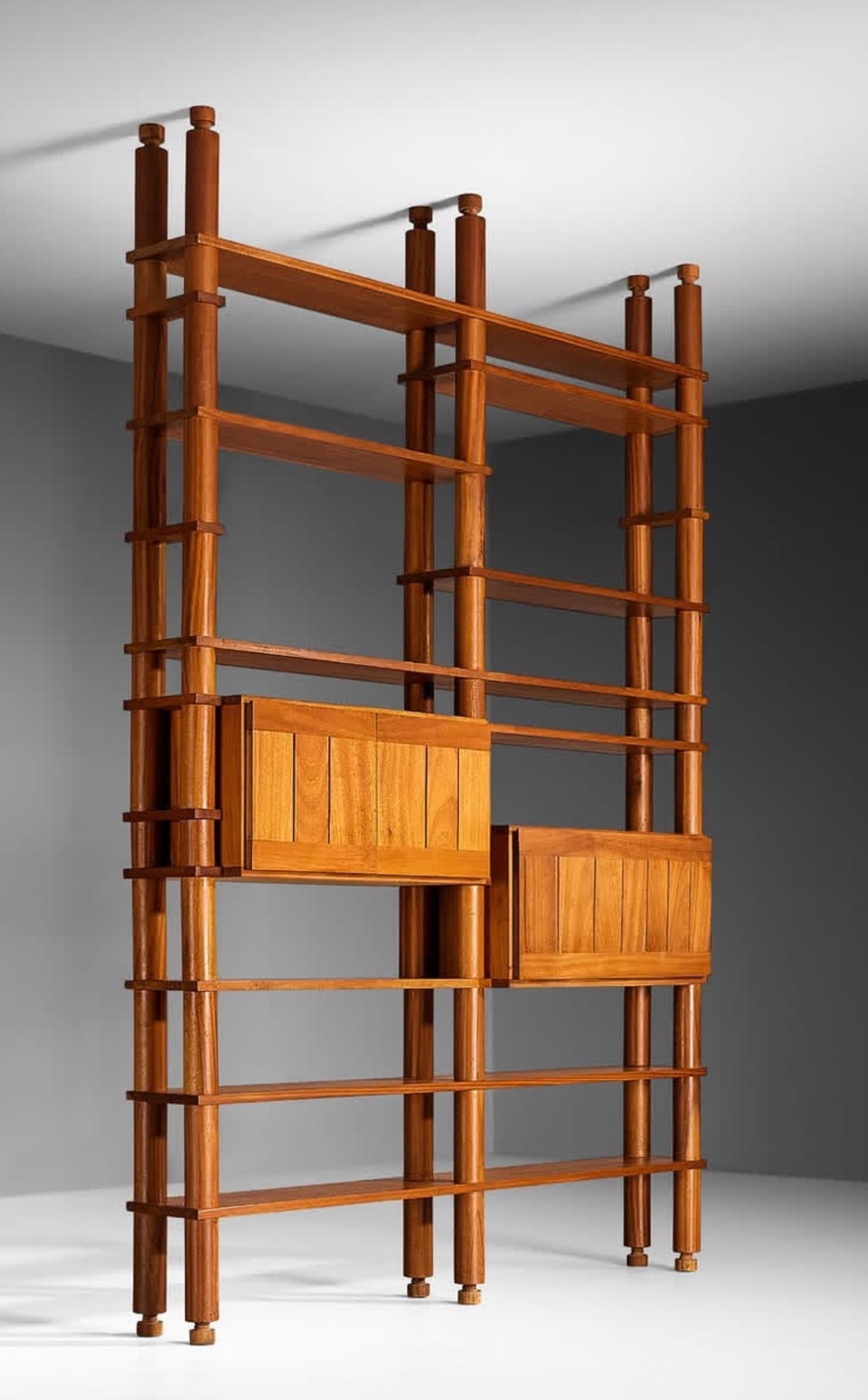 A tall, free-standing shelving system crafted from teak wood, featuring multiple open shelves and two integrated closed cabinet modules. The structure is defined by cylindrical vertical posts with turned finial details at the top and bottom, which support adjustable or fixed horizontal shelves. The cabinet fronts feature vertical slatted panels, contributing to its mid-century Italian aesthetic. — 3D model
