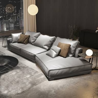 A modern L-shaped sectional sofa upholstered in a light grey leather or high-quality faux leather, featuring plush, soft cushions and contrasting accent pillows. The sofa has a low-profile design with distinct piping along the edges of the cushions and frame. — 3D model