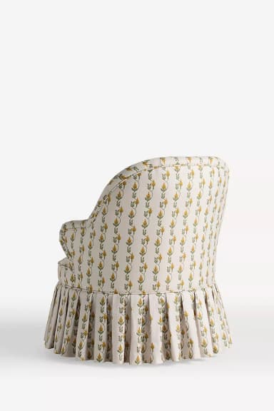 An upholstered armchair with a rounded back, rolled arms, and a pleated skirted base, covered in a cream fabric with a yellow and green botanical pattern. — 3D model
