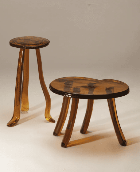 A compact, three-legged stool featuring a round, slightly dished seat and three organically curved legs, all crafted from a translucent, amber-toned resin material with subtle internal variations, giving it a depth of color. — 3D model