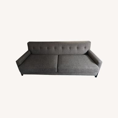A contemporary sofa upholstered in a heathered gray fabric, featuring a button-tufted backrest and flared, slightly sloped armrests. The sofa has two large seat cushions and is supported by short, dark block feet. — 3D model