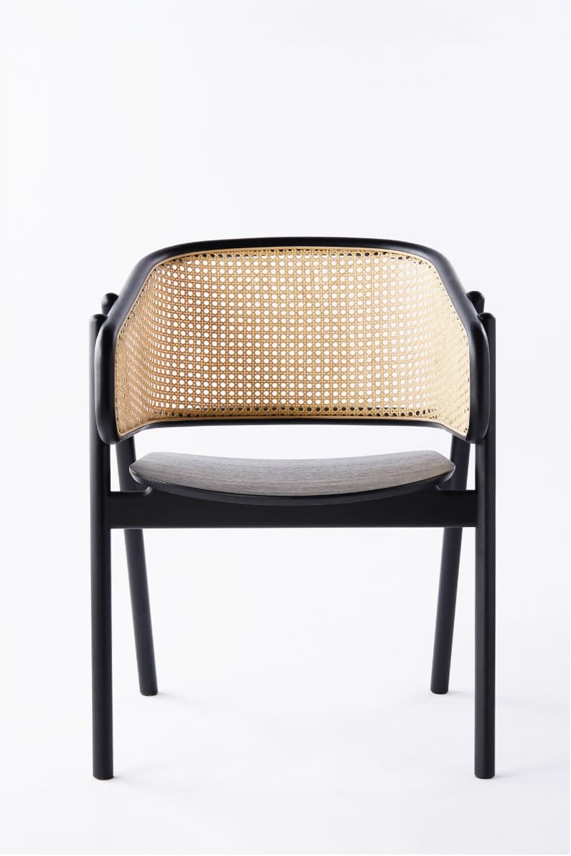 A modern armchair featuring a black finished solid wood frame, a natural cane woven backrest, and a light grey upholstered seat cushion. The chair has a sleek, minimalist design with integrated armrests that flow from the backrest. — 3D model
