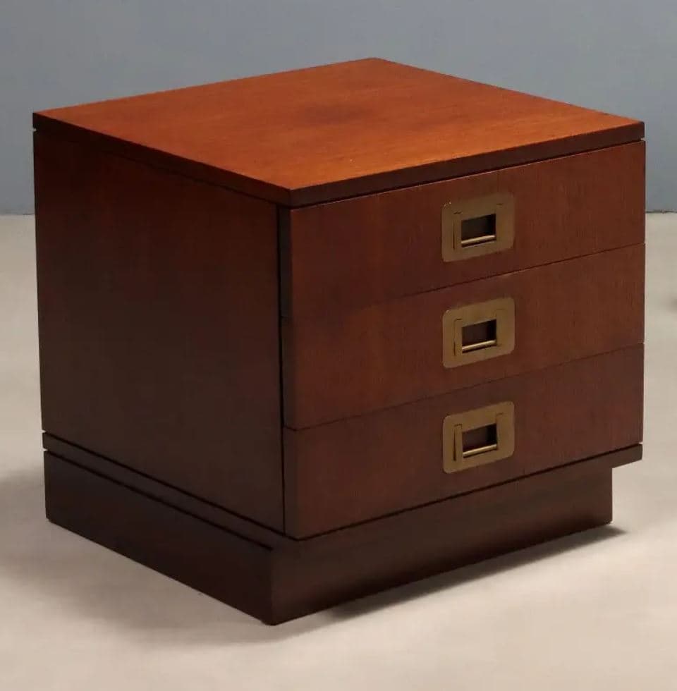 A compact, three-drawer wooden nightstand or side table, characterized by its reddish-brown finish and distinctive brass campaign-style recessed pull handles, supported by a recessed plinth base. — 3D model