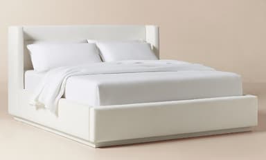 A contemporary upholstered platform bed featuring a clean, minimalist design. The headboard has subtle wingback sides that angle slightly outwards, providing a comfortable backrest. The entire frame, including the headboard and side rails, is covered in a light-colored, possibly linen-blend, fabric. The bed is designed for a mattress to sit directly on the platform, eliminating the need for a box spring. It is presented with white bedding. — 3D model