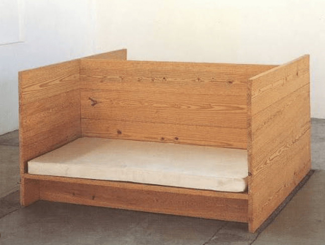 A minimalist bed frame crafted from light-toned wood, featuring high, solid panel sides and a lower footboard and headboard. It includes a simple white mattress, and the overall design suggests a toddler or child's bed with a low profile. — 3D model