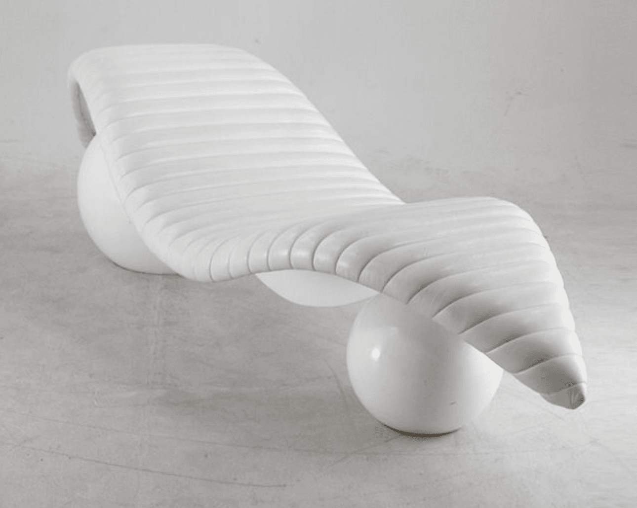 A contemporary white chaise lounge with a distinctive sculptural design. The seating surface is elongated and features horizontal channel tufting, creating a ribbed effect. It is supported by two spherical bases, one positioned towards the front and the other towards the rear, providing an unusual and dynamic stance. The overall form is organic and flowing. — 3D model