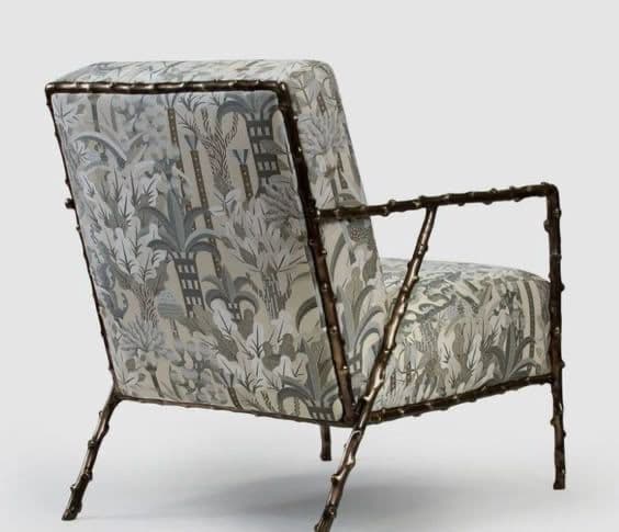 A single armchair with a distinctive frame structure resembling bamboo stalks and a patterned fabric upholstery. The armchair features a high back, armrests, and four legs, all constructed with a metallic frame that mimics organic growth patterns. The fabric is adorned with a dense, repeating motif of tropical foliage and possibly architectural elements in shades of grey, white, and blue. — 3D model