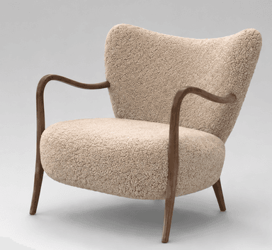 An armchair featuring a rounded, plush silhouette upholstered in a cream or beige bouclé fabric. It has visible, smoothly curved dark wooden armrests that extend downwards to form the front legs, and splayed wooden back legs. The backrest is slightly flared, providing a comfortable seating experience. — 3D model