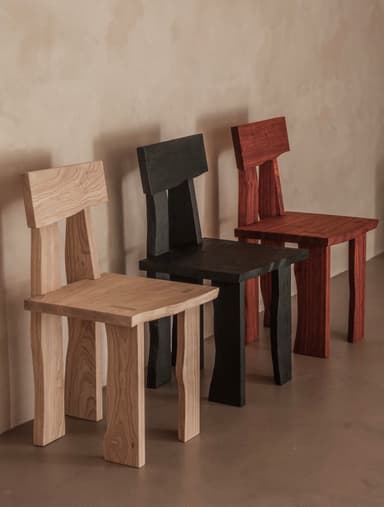 A minimalist accent chair constructed from light-toned solid wood, featuring a blocky and robust design. The chair has a square seat and a rectangular backrest that is attached with two vertical supports. The four legs are thick and subtly curved, contributing to a rustic yet modern aesthetic. The natural wood grain is visible throughout the piece, emphasizing its material and simple construction. — 3D model