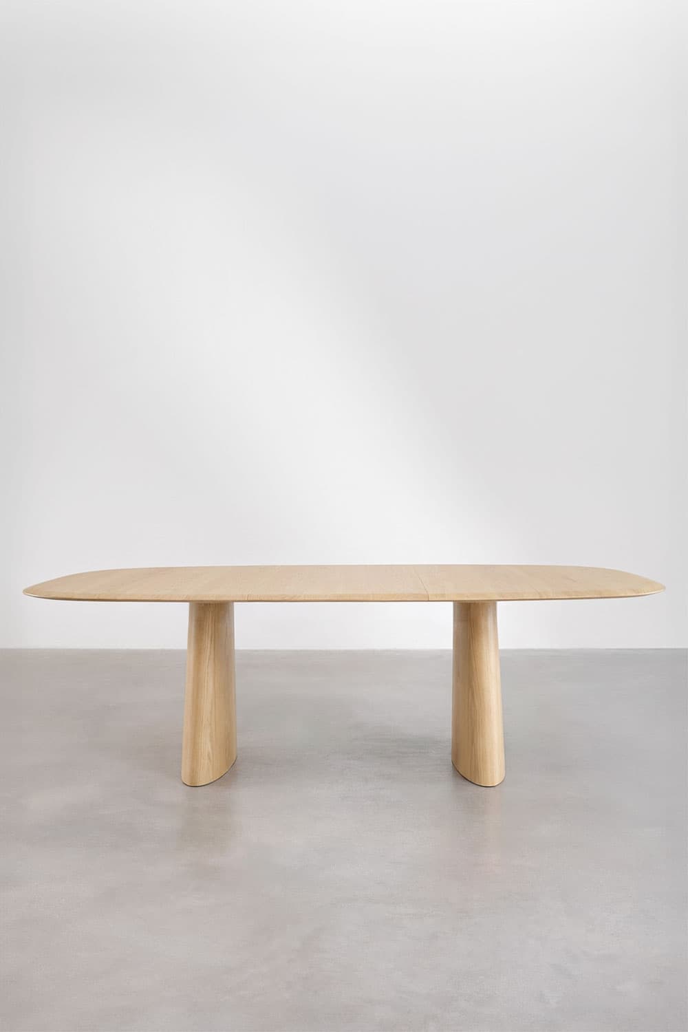 A minimalist dining table featuring an elongated oval tabletop crafted from light-toned wood, likely oak or ash. The tabletop has smoothly rounded edges, creating a soft, inviting profile. It is supported by two substantial, sculptural pedestal bases, also made of solid wood, which are broad at the top and taper slightly towards the bottom, presenting a robust yet elegant foundation. The table's design emphasizes clean lines and organic forms, characteristic of contemporary and minimalist aesthetics. — 3D model