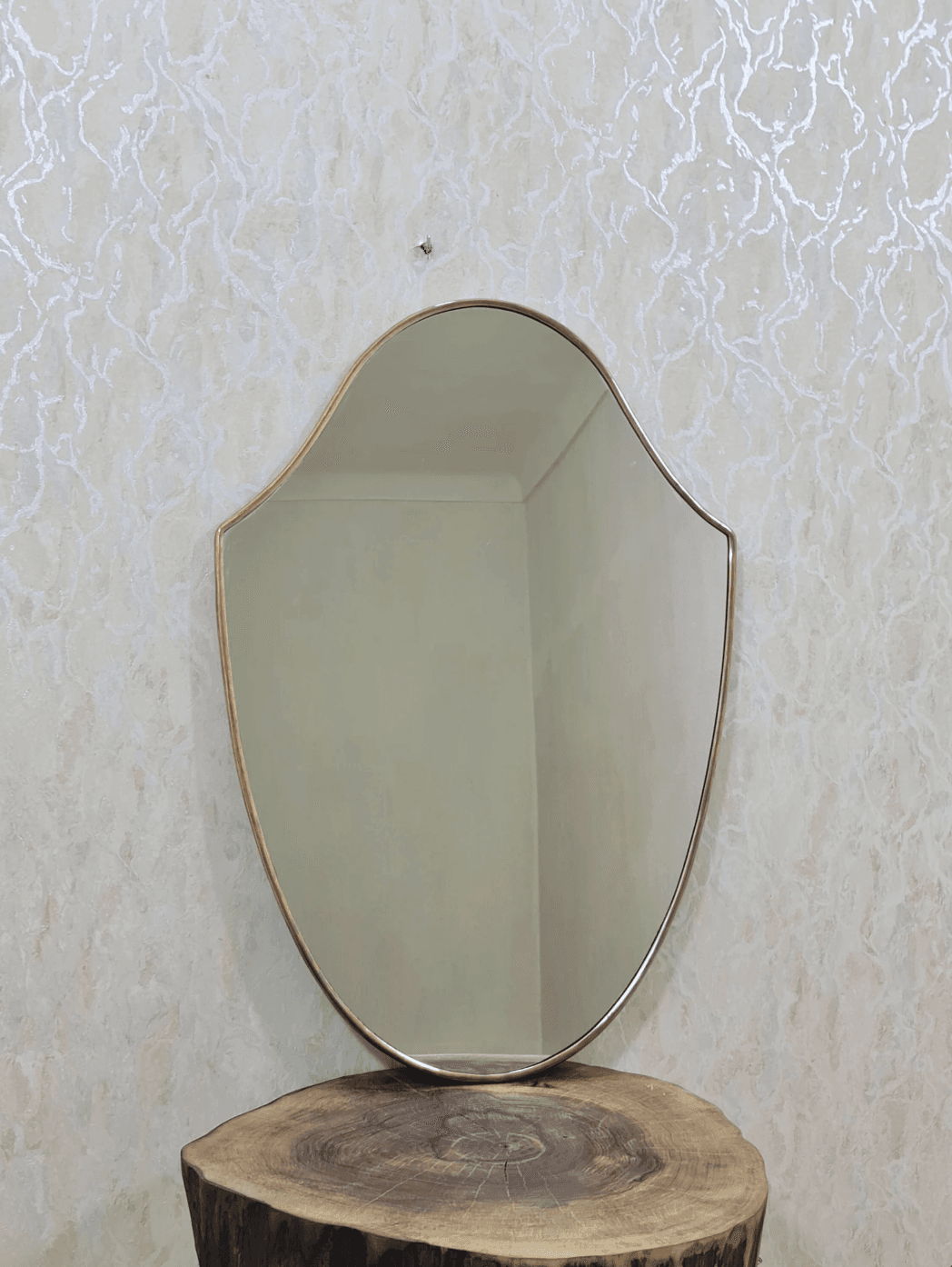A wall-mounted mirror featuring a distinctive scalloped, shield-like silhouette. The mirror is framed by a slender, polished brass border, giving it an elegant and classic appearance. The glass surface reflects light, and the overall design suggests a blend of traditional and contemporary aesthetics. — 3D model