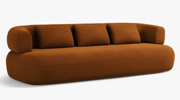 A contemporary sofa with a low profile and rounded edges. It features a solid base and a curved backrest. Three loose square cushions are placed against the backrest for added comfort. The overall design is minimalist and modern. — 3D model