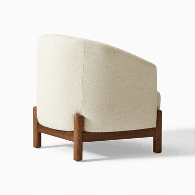 A modern armchair upholstered in a textured, light-colored fabric. It features a gently curved backrest that extends to armrests. The chair is supported by a dark wood frame with distinct legs that are cylindrical at the bottom and square where they meet the seat. — 3D model