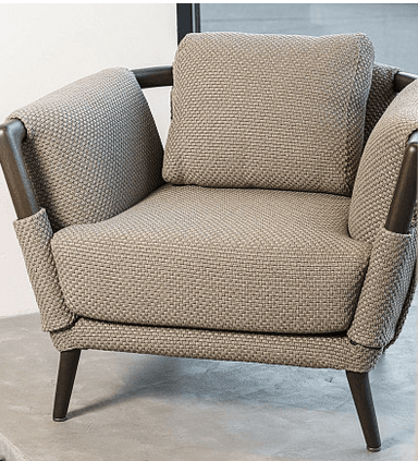 A contemporary armchair with a fabric-covered frame, featuring a textured weave. It has a prominent wooden frame visible at the arms and back, with tapered wooden legs. A square throw pillow rests on the seat. — 3D model