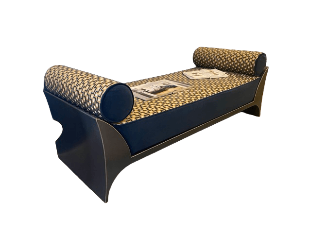 A long, upholstered bench with a dark blue base and a patterned cushion. It features two cylindrical bolster pillows at either end, upholstered in a fabric with a geometric pattern of interlocking gold and dark blue shapes. The base has a sleek, modern design with curved, flared legs. Two magazines are placed on the seating surface. The overall design suggests a contemporary or Art Deco influence. — 3D model