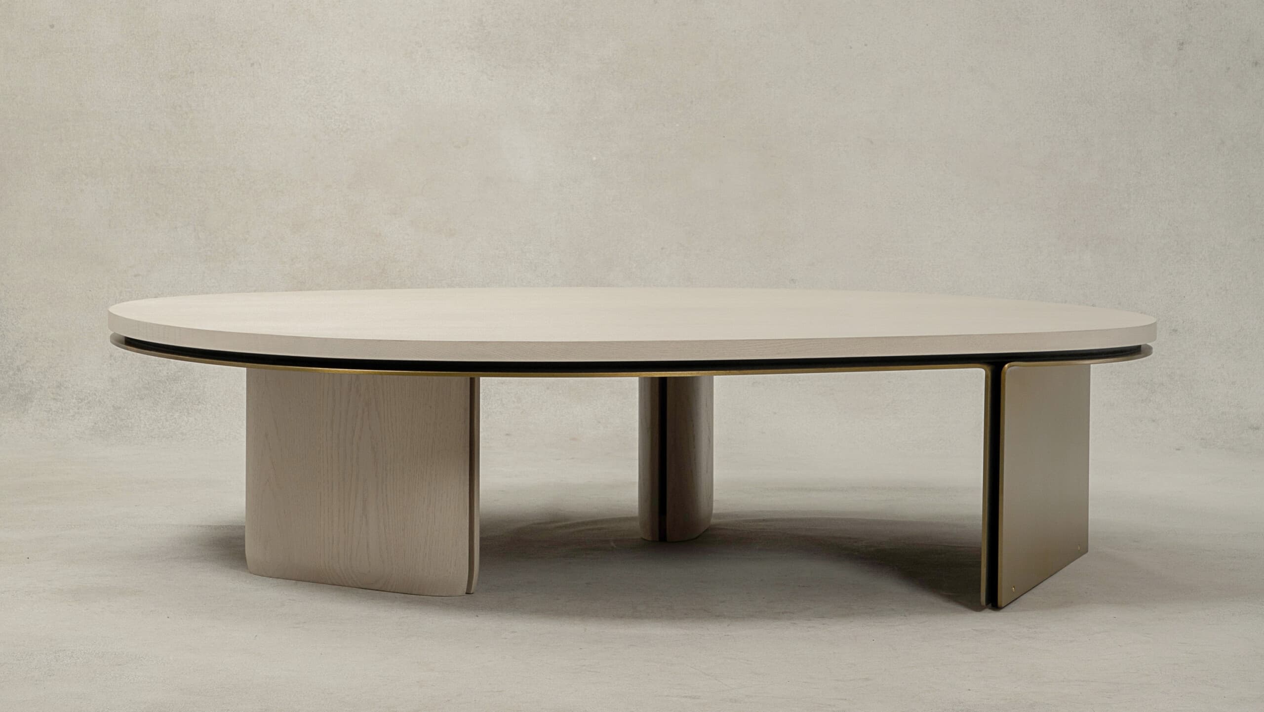 An oval coffee table featuring a light-toned wood veneer top with a thin dark edge and an integrated brass trim. The base combines two substantial, curved panel legs made of matching light wood and two outer, thin rectangular legs crafted from a brass-toned metal. The design is modern and minimalist. — 3D model