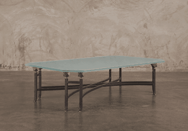 A low-profile table featuring a frosted glass top with an octagonal shape, supported by a wrought iron base with intricate curved and intersecting elements. Decorative brass finials connect the glass top to the metal base. — 3D model