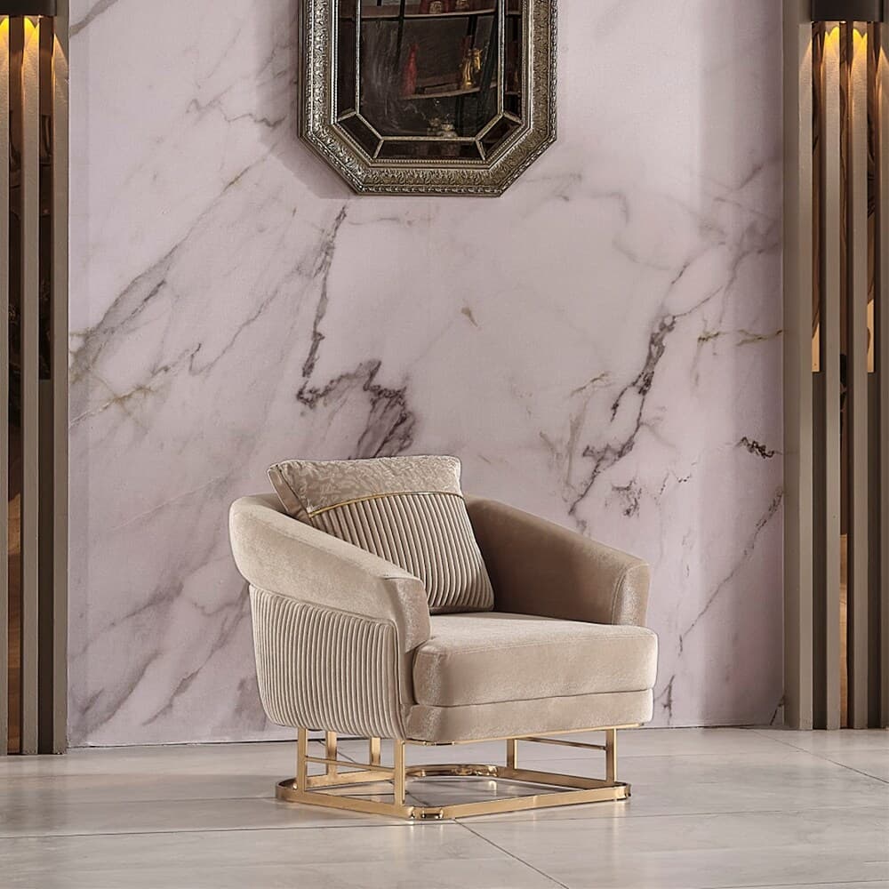 A contemporary armchair featuring soft, light brown velvet upholstery with a distinctive fluted or reeded pattern on its backrest and the outer sides of its curved armrests. The chair is supported by a sleek, rectangular gold-finished metal base. It includes a loose back cushion, also upholstered in velvet, with a contrasting patterned fabric panel and a gold trim detail. — 3D model