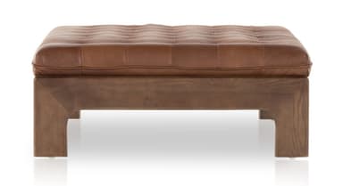 A rectangular tufted ottoman with a dark wood frame and brown leather upholstery. The frame features a modern design with angular legs and horizontal supports. Leather straps are integrated into the frame to hold the cushion in place. The cushion is deeply tufted with visible stitching. — 3D model
