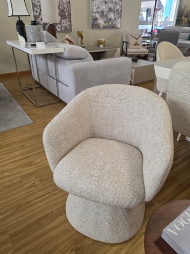 A contemporary barrel-shaped swivel accent chair, fully upholstered in a light beige or cream textured fabric. The chair features a rounded back and seat that merge seamlessly, resting on a cylindrical, fully upholstered base that conceals a swivel mechanism. The design is compact and modern, suitable for various interior settings. — 3D model