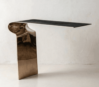 A sleek, modern cantilevered console table featuring a dark rectangular top and a single, curved, textured brass base. — 3D model