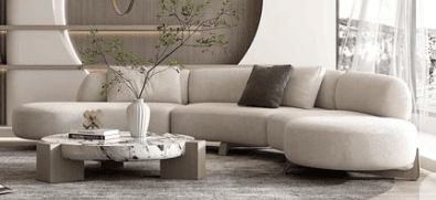 A light beige or cream-colored curved modular sectional sofa, composed of multiple upholstered segments that form a continuous, flowing seating arrangement. It features soft, rounded lines, low armrests integrated into the back, and discreet, tapered legs. A dark grey accent pillow is placed on one of the segments. — 3D model