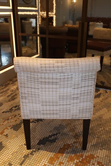 An armless dining chair featuring a light, patterned fabric upholstered back and frame, contrasted with a smooth, warm brown leather seat cushion. The chair stands on four dark, slightly tapered wooden legs. — 3D model