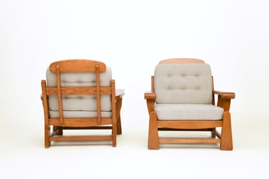 A pair of lounge chairs, each featuring a robust wooden frame with light-colored upholstered seat and back cushions. The back cushions are tufted with six buttons. The chairs display a sturdy, classic design with prominent wooden armrests and base structure. — 3D model