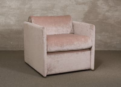 A plush armchair upholstered in a soft, textured fabric. It features a boxy silhouette with wide, flat arms and a low back. The seat cushion is deep and appears generously padded. A single, matching lumbar pillow is placed against the backrest. The armchair is presented against a textured, neutral-toned wall and floor. — 3D model