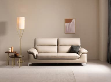 A light beige leather sofa with two seat cushions and a tufted seat base. It features a contemporary design with slightly sloped arms and a single row of tufting across the seat. The sofa is supported by slender metal legs. A single dark grey throw pillow with a textured pattern rests on the right seat cushion. — 3D model