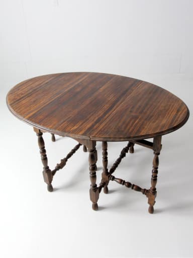 A traditional dark-stained wood drop-leaf gateleg table with an oval top. The base features turned baluster-style legs connected by elaborately turned and blocked H-stretchers. The leaves are hinged, allowing the table to be expanded or condensed. — 3D model