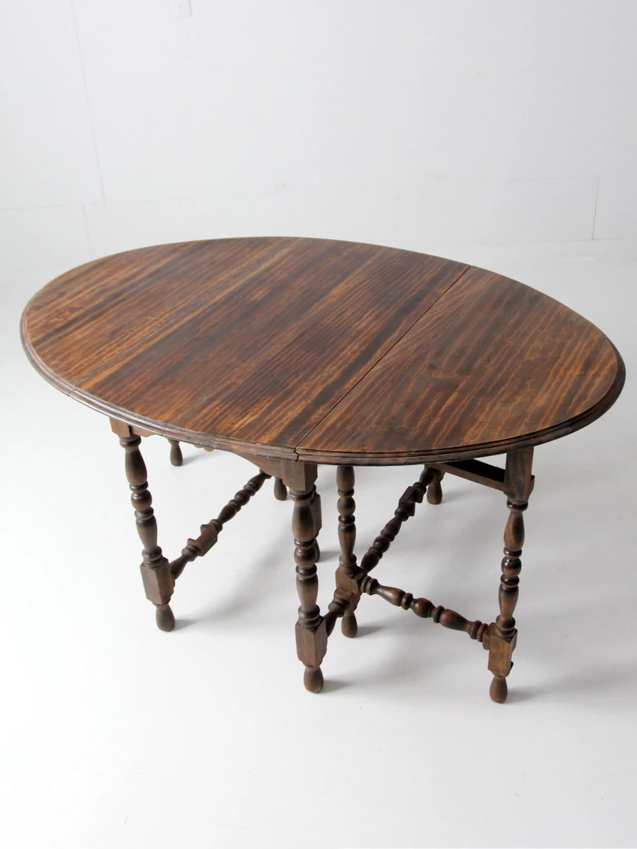 A traditional dark-stained wood drop-leaf gateleg table with an oval top. The base features turned baluster-style legs connected by elaborately turned and blocked H-stretchers. The leaves are hinged, allowing the table to be expanded or condensed. — 3D model