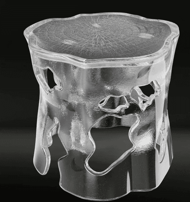 A sculptural accent table or stool crafted from clear, textured resin, designed to resemble a block of ice or a natural tree stump. The piece features an organic, irregular silhouette with cut-out sections in its body, giving it a light, ethereal appearance. Embedded within the clear material are small, delicate golden leaf inclusions. The top surface is flat but textured with an embossed wood grain pattern, suggesting tree rings, further enhancing its nature-inspired aesthetic. The overall impression is one of modern artistry combined with natural elements. — 3D model