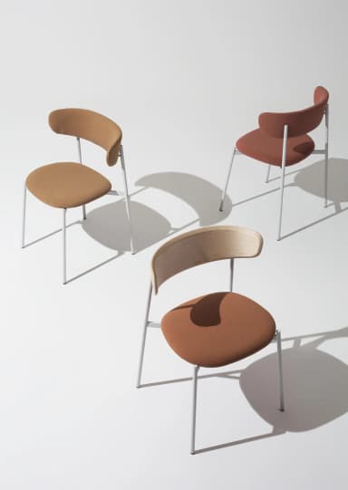 A modern dining chair with a bentwood backrest and a fabric-upholstered seat, supported by a slender, light gray metal frame. The backrest exhibits a natural wood grain pattern and a curved silhouette. The seat is padded and covered in a textured, tan-colored fabric. The frame consists of four thin, cylindrical legs connected by a horizontal support structure under the seat, all finished in a matte light gray. — 3D model