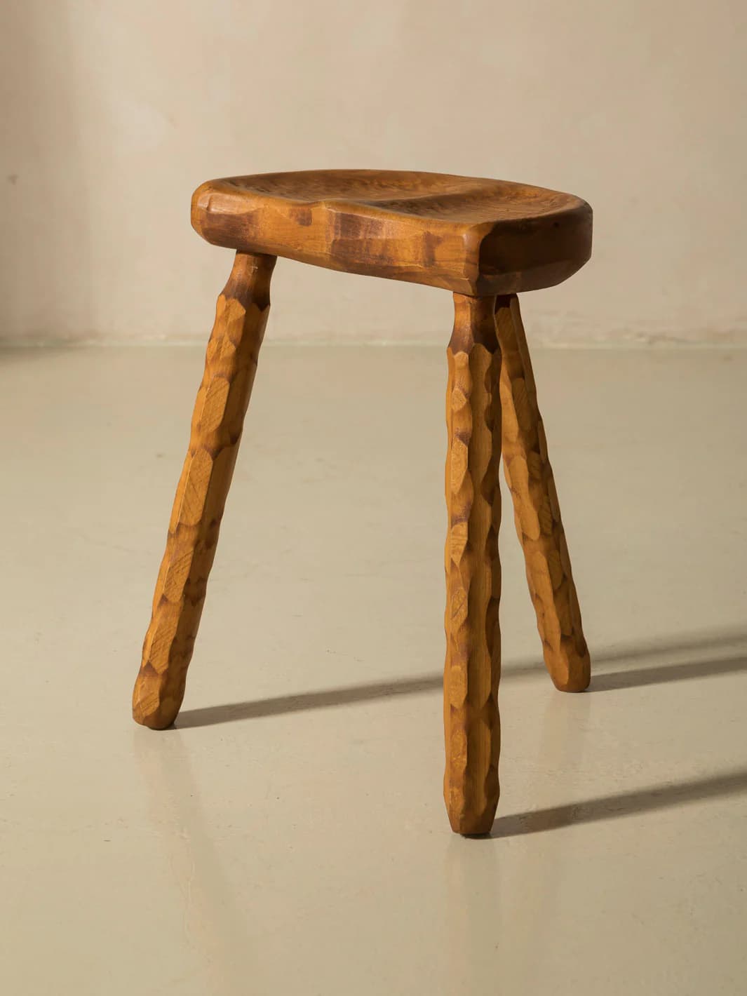 A three-legged wooden stool with an oval, contoured seat. The legs are carved with a textured pattern, giving them a rustic appearance. The overall design is simple and organic. — 3D model