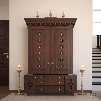 A dark brown wooden structure designed as a traditional Indian Pooja Mandir. It features an upper cabinet with double doors, intricately perforated with small cutouts and adorned with hanging brass bells. The top is accented with decorative brass finials. The lower section includes multiple storage drawers and two side compartments, each featuring a carved floral or geometric pattern. The overall aesthetic is rich and traditional, suitable for religious ceremonies. — 3D model