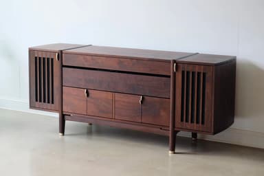 A long, low, dark wooden cabinet with a distinct mid-century modern design. It features slatted sections on the curved ends, a central open shelf, and multiple drawers and cabinet doors below, all adorned with small brass pull handles. The cabinet is supported by angled, tapered legs with brass ferrules at the bottom. — 3D model