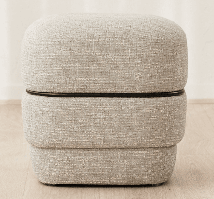 A contemporary, rectangular upholstered ottoman featuring a stacked, three-tiered design. The entire piece is covered in a light gray, highly textured fabric. A thin, dark (likely black) accent band visually separates the top cushion from the middle section, adding a distinct linear detail. The ottoman has soft, rounded edges and a minimalist aesthetic. — 3D model